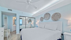 A bedroom with a large bed, a ceiling fan, and a view of the ocean through a sliding door. - Beachfront Corner Views, Indoor & Outdoor Pools, Walk to Dining | BEACHBALL PROPERTIES (Orange Beach)