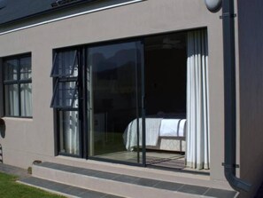 A modern building with large sliding glass doors leading to a bedroom with a bed and curtains. - Worcester the Karoo Guestrooms (Altona, Worcester)