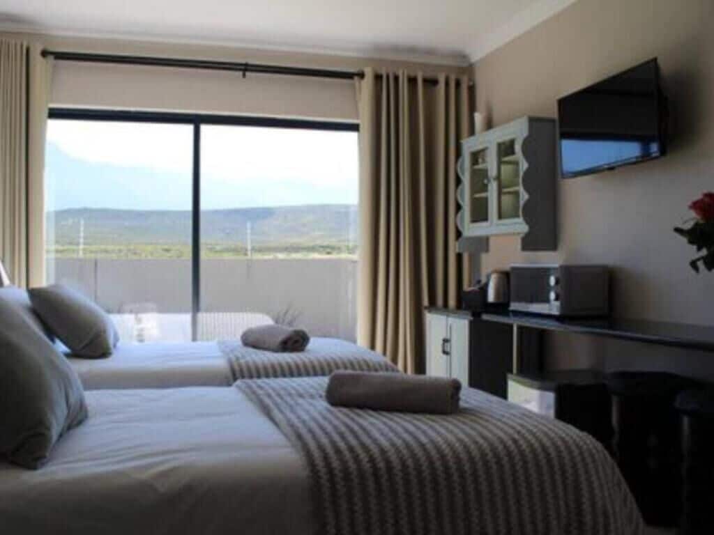 A hotel room with two beds, a television, a desk, and a view of the landscape.