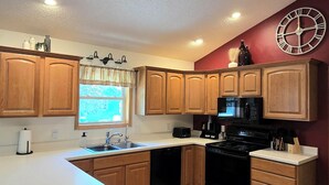 A kitchen with wooden cabinets, a black stove, a microwave, and a clock on the wall.