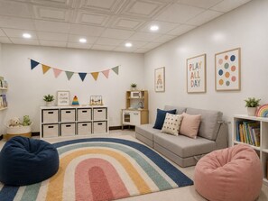 Habitación pensada para niños, con zona de juegos, sofá, pufs y juguetes educativos.
