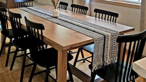 A dining area with a wooden table, black chairs, a woven table runner, and a hanging light fixture.