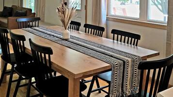 Un coin repas avec une table en bois, des chaises noires, un chemin de table en tissu tissé et un luminaire suspendu.