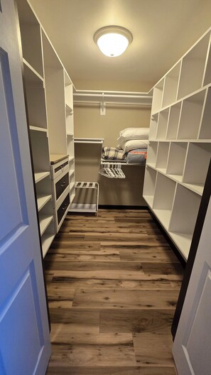 Un vestidor estrecho con piso de madera, estantes blancos y una barra para colgar ropa.