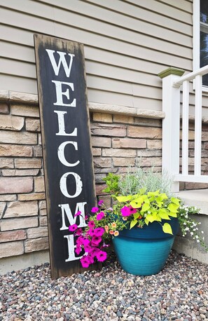 A wooden welcome sign with large white letters against a beige wall.