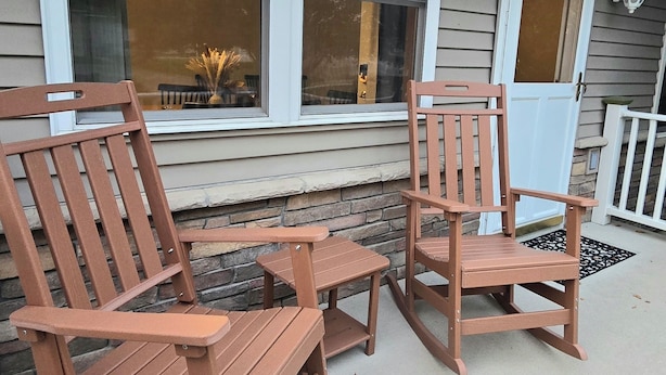 A porch with two rocking chairs and a small table, a window with a light fixture, and a door with a light fixture.