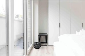 Ein modernes Zimmer mit einer Schiebeglasdoor, einem kleinen Tisch, einem schwarzen Korb und einem weißen Sofa.