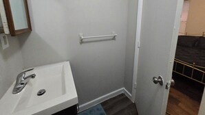 Un bany amb un rentapeus, mirall, prestatge per a tovalloles i una porta que dona a una altra habitació.