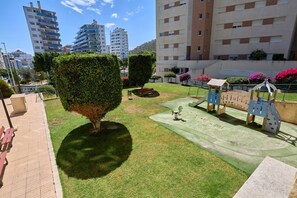 Un patio con un parque infantil, setos bien cuidados y una banca.