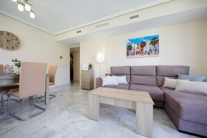 Ein Wohnzimmer mit einer Couch, einem Couchtisch, einem Essbereich mit Stühlen, einer Uhr und einem Bild an der Wand.