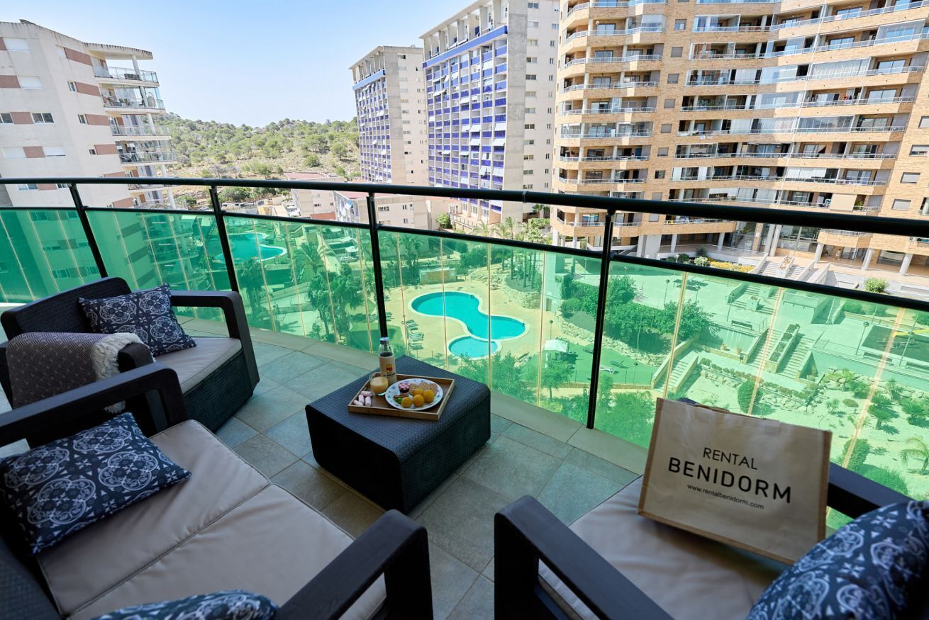 A balcony with outdoor seating, a tray with food and drink, and a sign for 'RENTAL BENIDORM.'