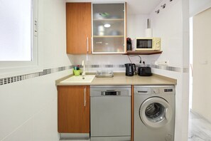 Cozinha compacta equipada com máquina de lavar louça, máquina de lavar roupa, micro-ondas e um armário com porta de vidro.