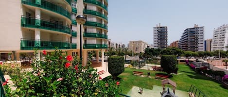 Un edificio residencial de varios pisos con balcones, un jardín bien cuidado y un cielo despejado.