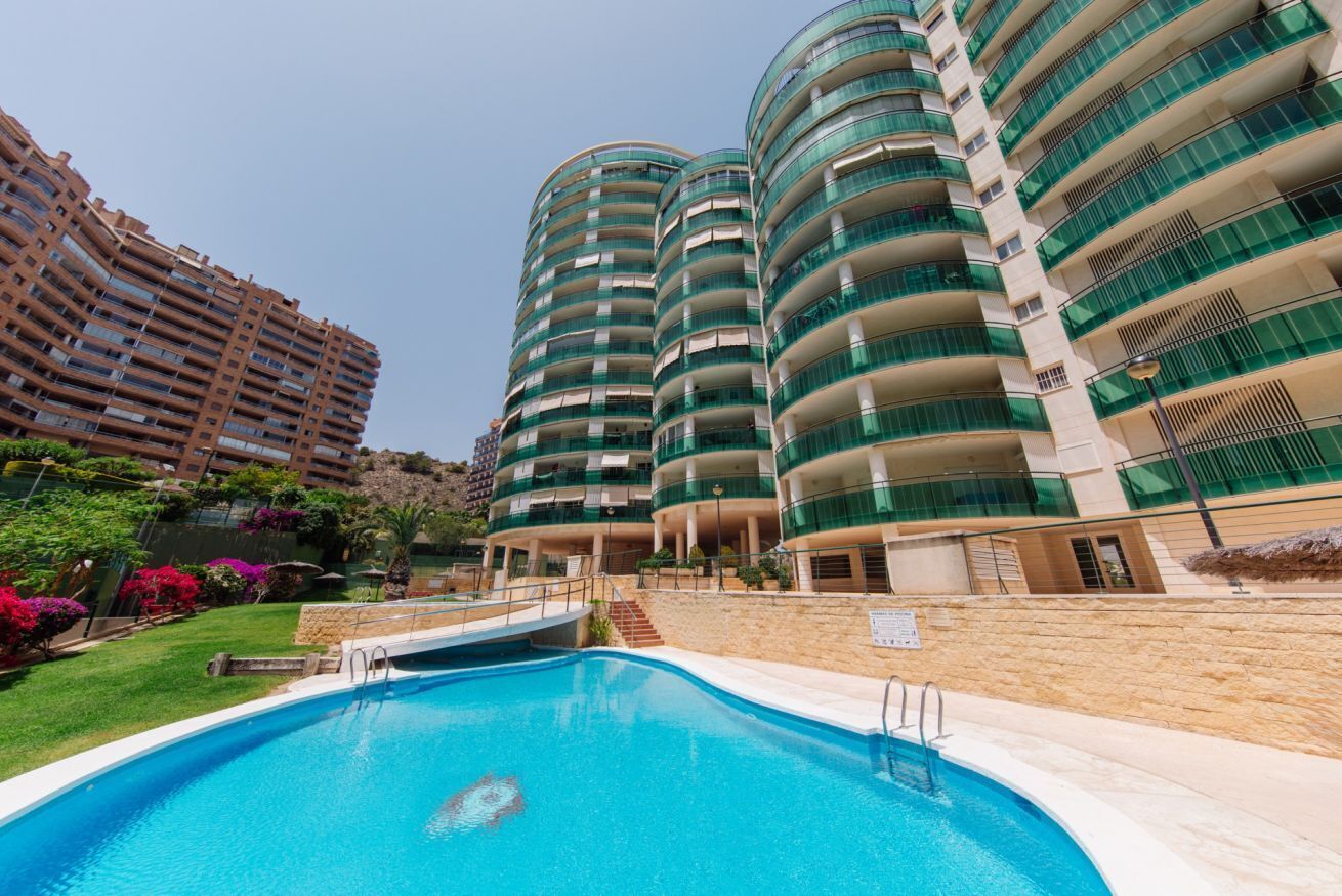 A modern hotel with a swimming pool, multiple balconies, and lush landscaping.