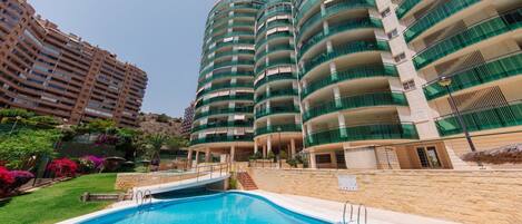 A modern hotel with a swimming pool, multiple balconies, and lush landscaping.