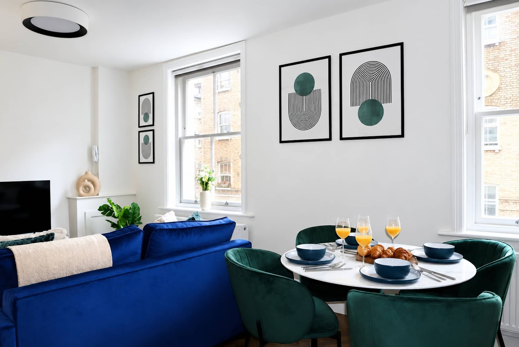A modern living room with a blue sofa, a dining table with blue chairs, and artwork on the wall.