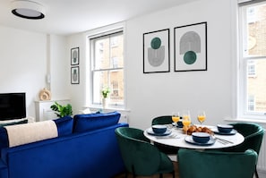 Ein modernes Wohnzimmer mit einem blauen Sofa, einem Esstisch mit blauen Stühlen und Kunstwerken an der Wand.