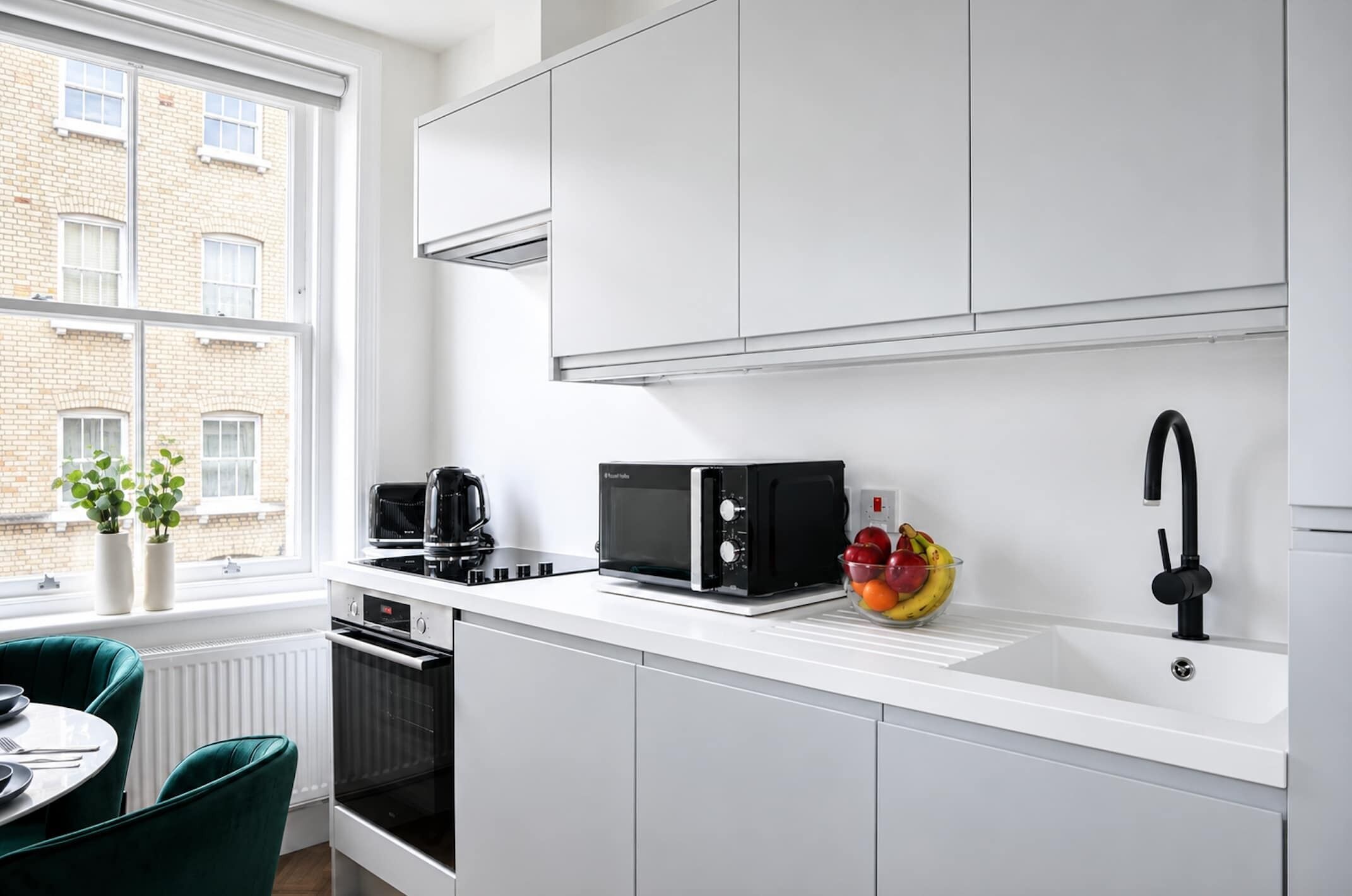 A modern kitchen with white cabinetry, a black microwave, a coffee maker, and a fruit bowl on the counter.