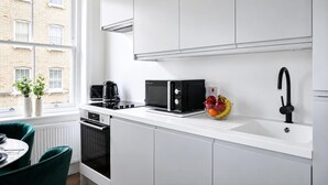 Una cuina moderna amb armaris blancs, un microones negre, una cafetera i un plat de fruita al taulell.