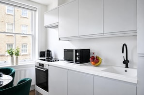 Eine moderne Küche mit weißen Schränken, einer schwarzen Mikrowelle, einer Kaffeemaschine und einer Obstschale auf der Arbeitsfläche.