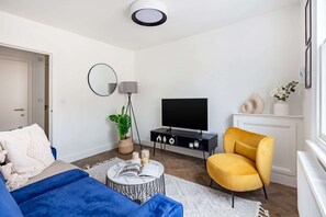 A modern living room with a sofa, a yellow armchair, a TV, a lamp, and a potted plant. - Cosy 1BR Flat Between Barbican & Old Street (London)