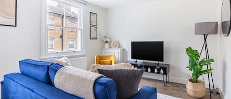A modern living room with a blue sofa, a flat-screen TV, a floor lamp, and a potted plant.