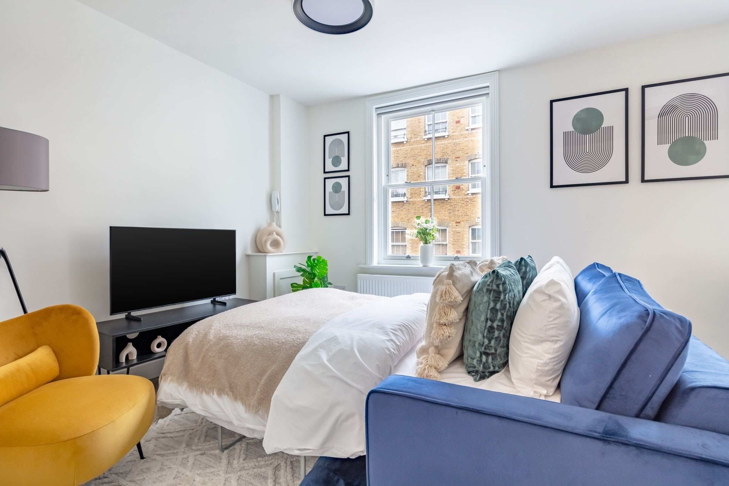 Une chambre moderne avec un lit, un canapé, une télévision et des œuvres d’art accrochées aux murs.