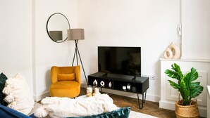Un salon moderne avec un canapé, un fauteuil jaune, un téléviseur, une lampe sur pied, une cheminée et une plante en pot.