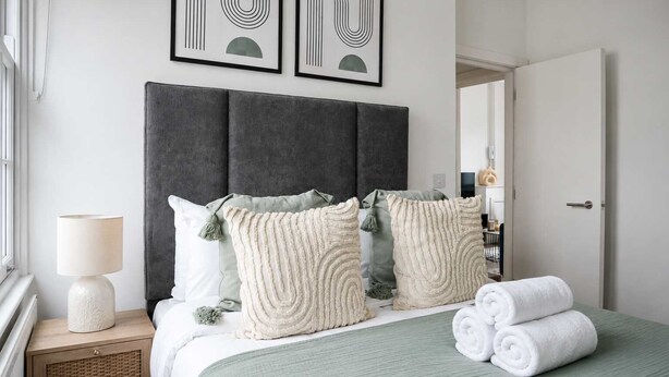 Un lit bien fait, avec des serviettes pliées, une lampe de chevet et des coussins décoratifs.