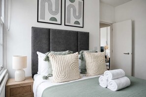 Ein ordentlich gemachtes Bett mit aufgerollten Handtüchern, einer Nachttischlampe und dekorativen Kissen.