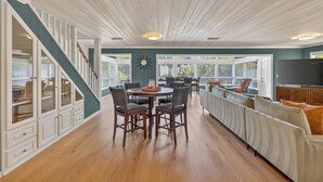 A spacious kitchen with wooden flooring, a dining area with chairs, a built-in bench, and a large window.