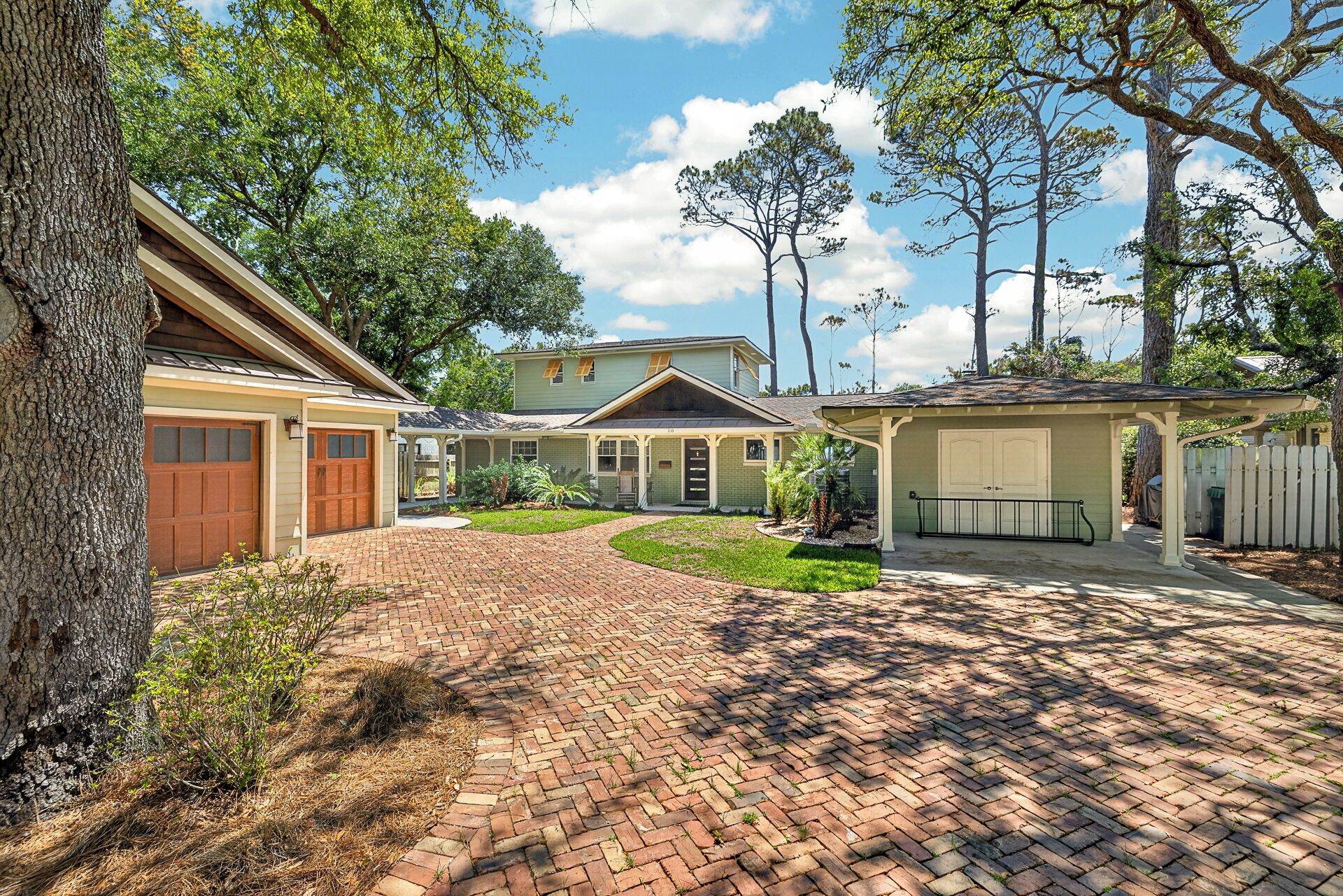 A residential property with a brick driveway, a covered porch, and a detached garage.