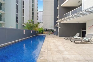 Ein Pool mit Liegestühlen, einem Sprungverbotsschild und Blick auf hohe Gebäude.