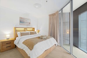 A bedroom with a large bed, a nightstand, a bedside lamp, and a view of the outside through a sliding glass door. - Urban Retreat 1Bed-1Bath-Study-Balcony-1Car (Brisbane City)