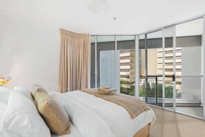Ein modernes Hotelzimmer mit einem großen Bett, Blick auf die Stadt durch raumhohe Fenster und einem Balkon.