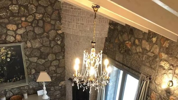 A living room with a stone wall, a chandelier, a sofa, a coffee table, and a flat-screen TV. - House Sleeps 6 With Pool (Chalcis)