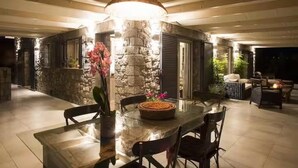 An outdoor dining area with a stone wall, a large pendant light, and a table with chairs. - House Sleeps 6 With Pool (Chalcis)
