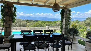 A covered patio with a pool, outdoor seating, and a view of mountains. - House Sleeps 6 With Pool (Chalcis)