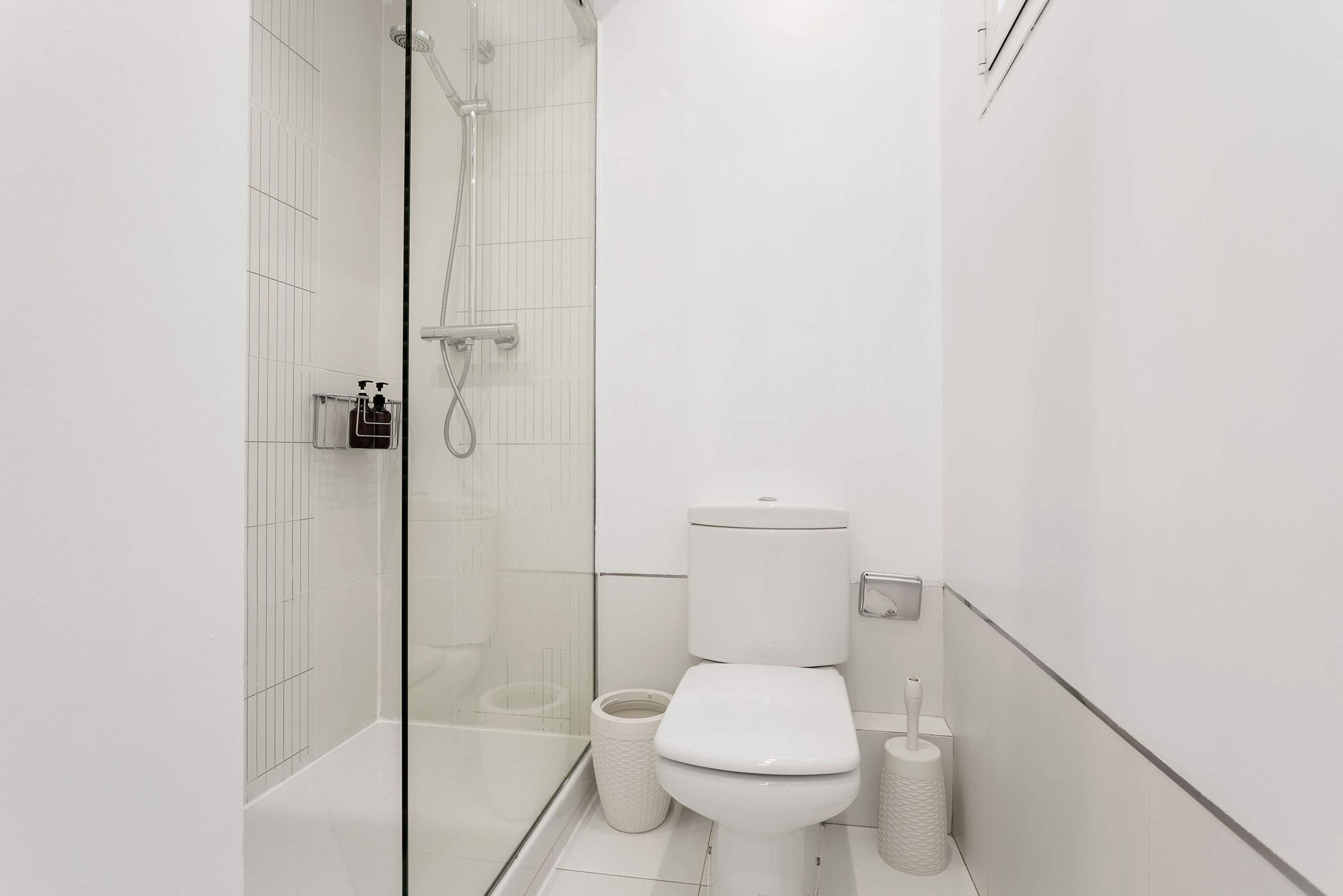 A modern bathroom with a glass shower enclosure, a toilet, and a trash bin.