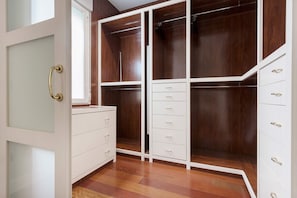 Ein begehbarer Kleiderschrank mit mehreren Schubladen und Regalen, Holzboden und eine weiße Tür mit goldener Klinke.