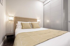 A bed with a beige bedspread, two pillows, and a headboard with a woven design. - Stylish 4BD Apartment Madrid Duque de Osuna II (Madrid)