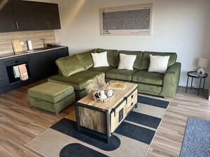 Una sala de estar moderna con un sofá verde, una mesa de centro de madera y una cocina al fondo.