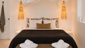 Un dormitorio con cama, dos lámparas de pared, una mesita de noche y un banco de mimbre con toallas.