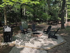 Un espace boisé comprenant un foyer, quatre fauteuils Adirondack et un petit abri de jardin.