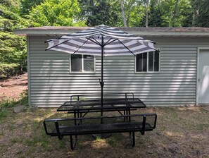 Un tavolo da picnic in metallo con un ombrellone a righe di fronte a una casa.