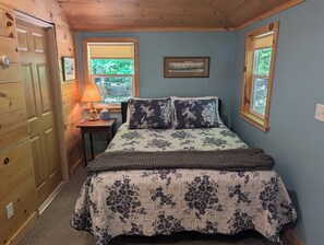 Una camera da letto con un letto, due finestre, un comodino, una lampada e una porta.