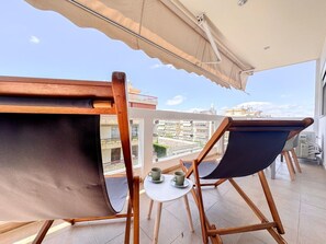 A balcony with two wooden chairs, a small round table, and a beige awning. - Bright Modern 1BR · 4-min Walk to the Sea · Alimos Riviera (Alimos)