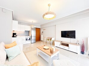 A modern living room with a sofa, coffee table, TV, and kitchen area. - Bright Modern 1BR · 4-min Walk to the Sea · Alimos Riviera (Alimos)