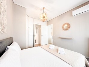 A hotel room with a bed, a bedside table, a wall-mounted air conditioner, and a decorative wall piece. - Bright Modern 1BR · 4-min Walk to the Sea · Alimos Riviera (Alimos)
