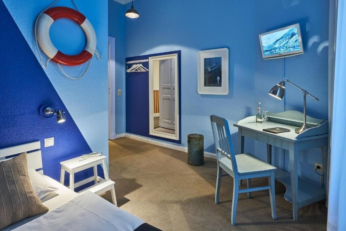 Una habitación con una cama, un escritorio con una silla, un televisor, un flotador salvavidas y una puerta.